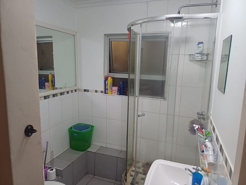 A functional bathroom featuring a corner shower enclosure, tiled walls and flooring, and a wall-mounted mirror above the basin area.