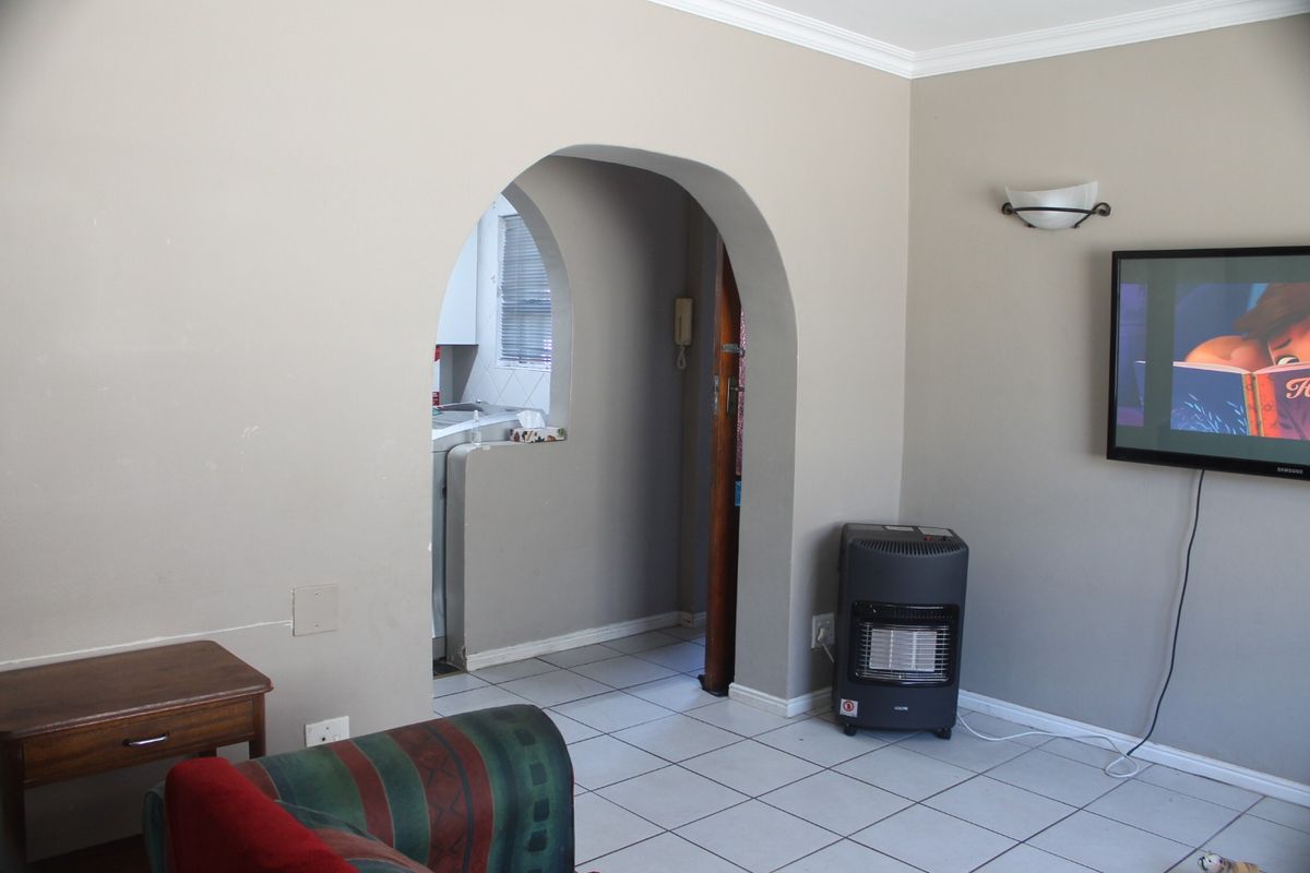 A living room featuring tiled flooring and a distinctive arched doorway leading to an adjacent space, with neutral wall tones and fixed lighting.