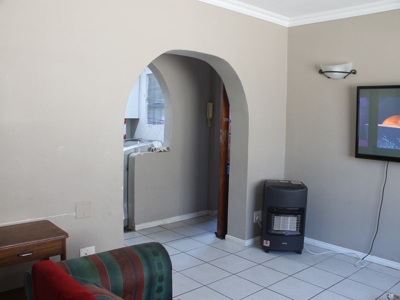 A living room featuring tiled flooring and a distinctive arched doorway leading to an adjacent space, with neutral wall tones and fixed lighting.