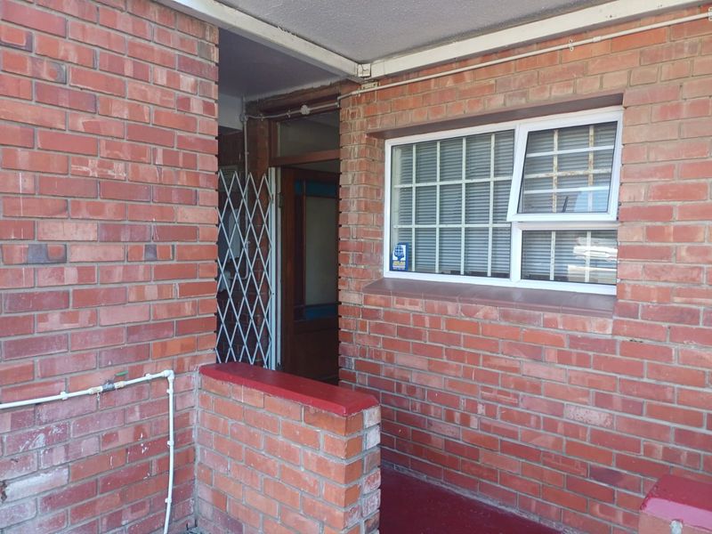 Exterior view of the apartment entrance featuring a brick facade, security gate, and window with security bars.