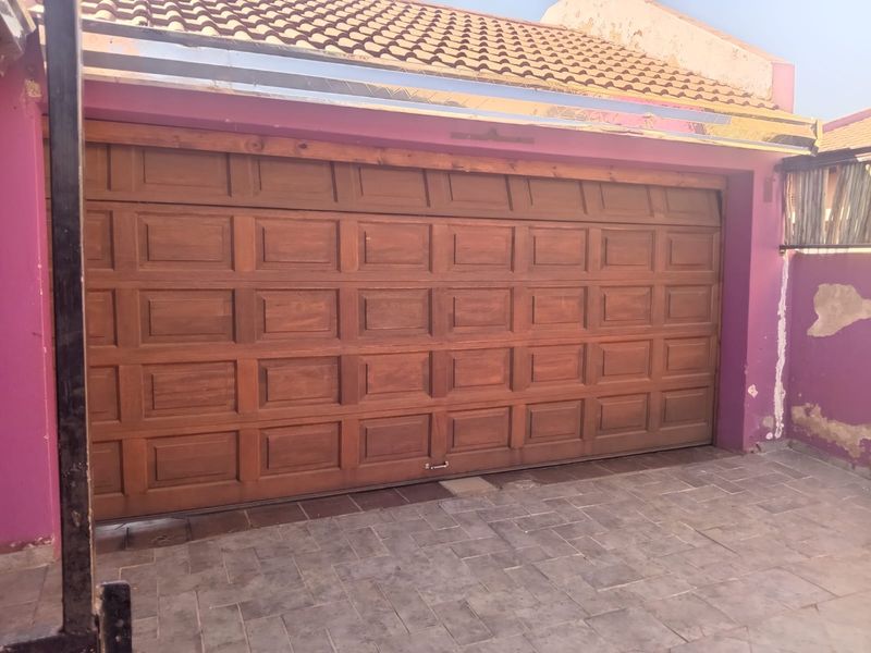 A single garage featuring a wooden sectional door, tiled roof, and paved driveway, with visible exterior wall maintenance required.