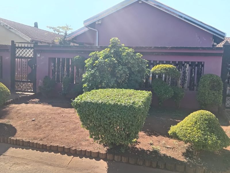 Front view of the property featuring a perimeter wall, metal gate, and a landscaped garden area with a tiled roof structure.