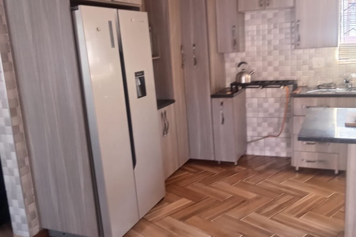 A functional kitchen featuring wood-look cabinetry, herringbone-patterned flooring, and a tiled backsplash, with an integrated layout and visible gas connection.