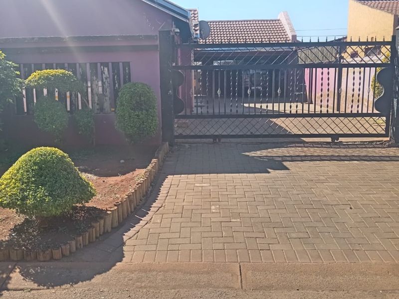 Front view of the property featuring a paved driveway, secure metal gate, and a tiled roof facade.