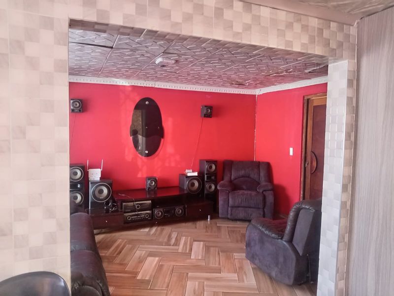Living room featuring tiled flooring, decorative ceiling tiles, and a tiled archway entrance. The space has a dated aesthetic and requires cosmetic updates.