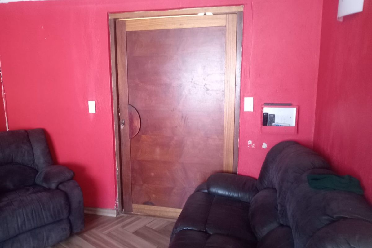 A living room featuring herringbone flooring and a wooden door, currently finished with bold red wall paint requiring cosmetic attention.