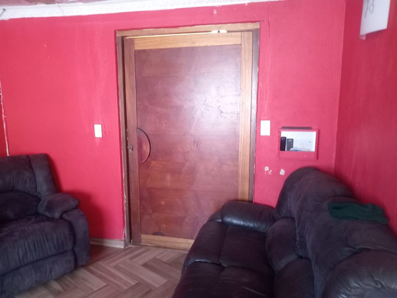 A living room featuring herringbone flooring and a wooden door, currently finished with bold red wall paint requiring cosmetic attention.