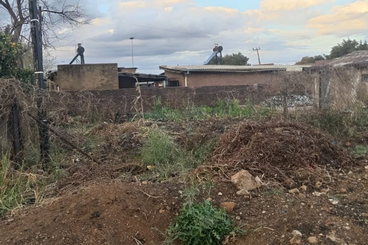 A rear view of the property showing a large unmaintained yard area with a brick boundary wall and solar water heating infrastructure visible.