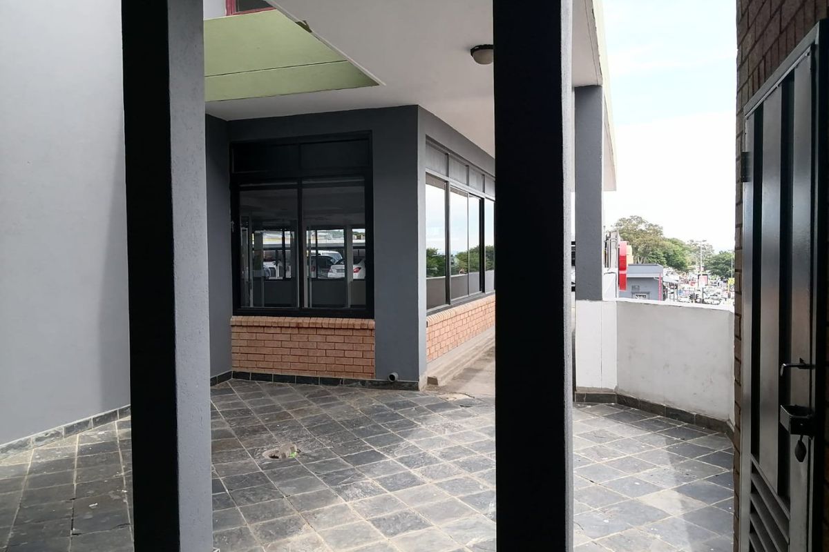 A covered outdoor patio area featuring tiled flooring, brick accents, and structural pillars, providing a functional transition space for the commercial property.