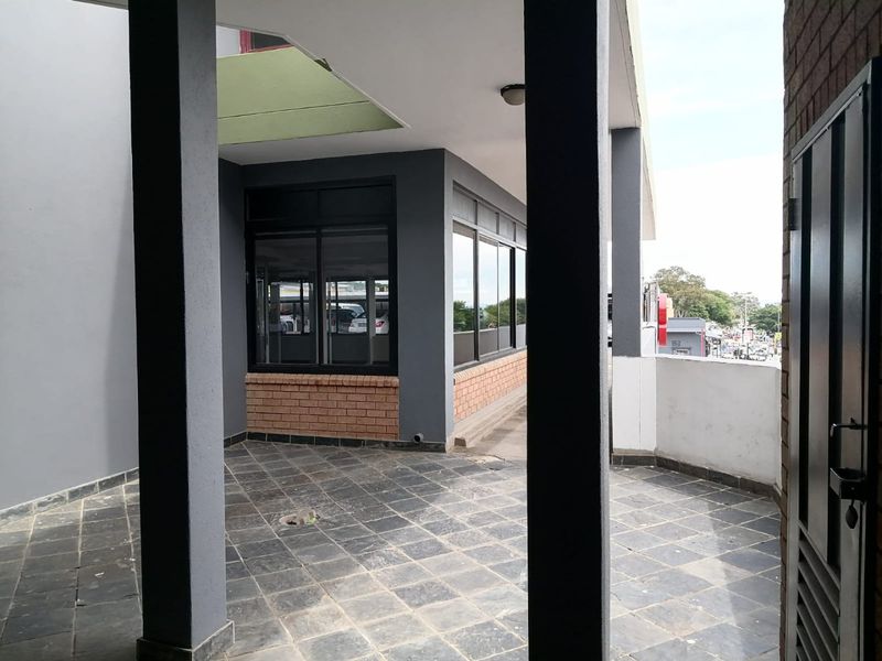 A covered outdoor patio area featuring tiled flooring, brick accents, and structural pillars, providing a functional transition space for the commercial property.