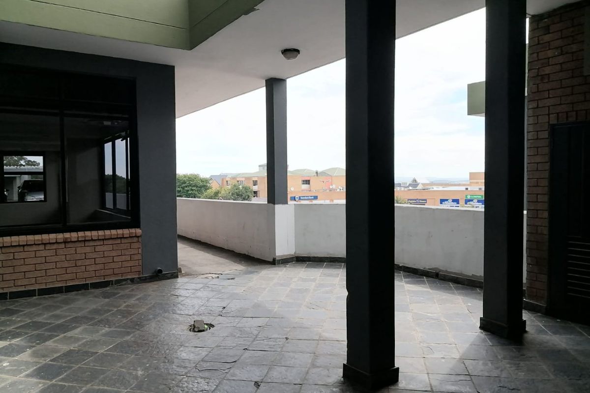 A spacious covered balcony area featuring stone tile flooring and structural columns, offering an open-air view of the surrounding commercial area.