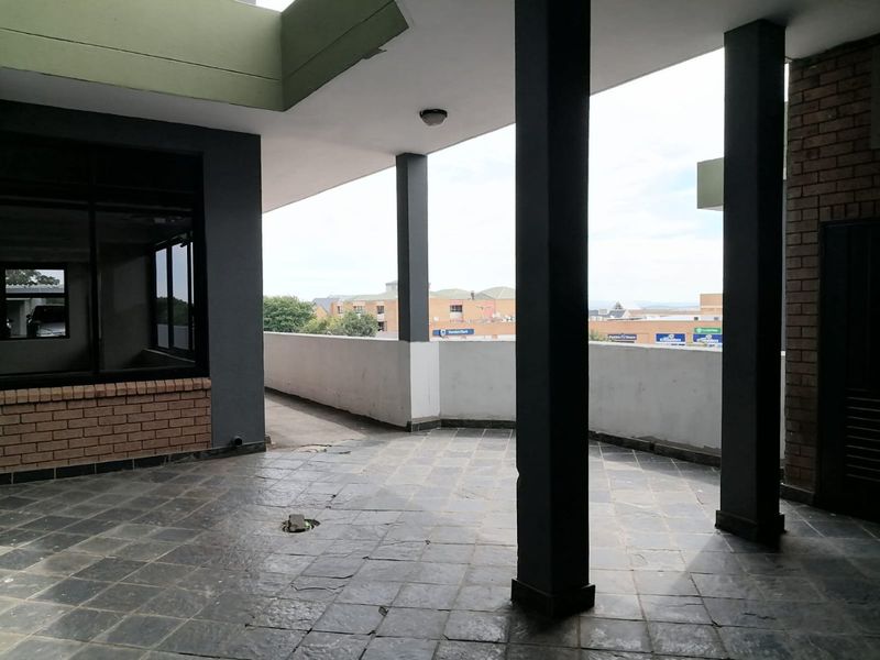 A spacious covered balcony area featuring stone tile flooring and structural columns, offering an open-air view of the surrounding commercial area.