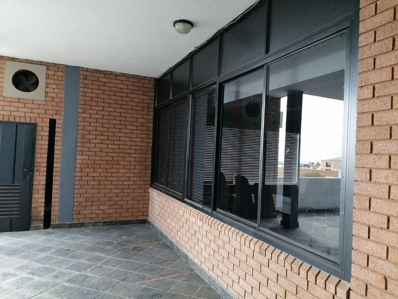 A covered outdoor patio area featuring exposed brick walls, dark tiled flooring, and large aluminium-framed windows overlooking the exterior.