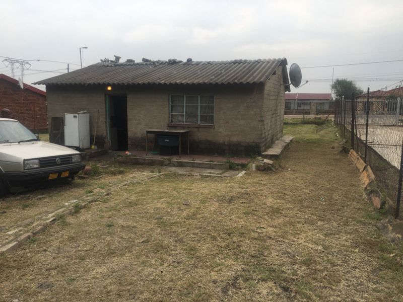 Rear view of a single-story detached house featuring a corrugated roof, steel window frames, and a fenced yard area.