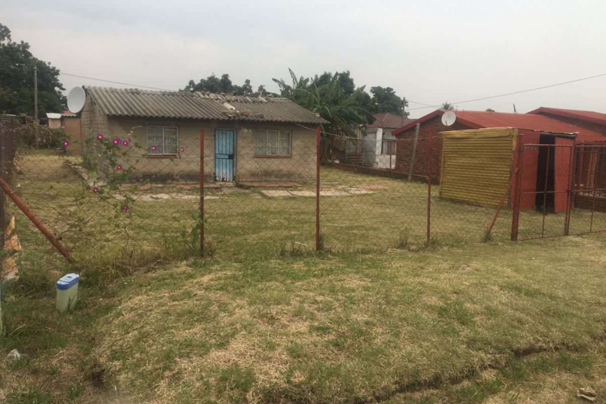 A detached residential property featuring a corrugated roof and fenced yard, showing signs of significant wear and requiring maintenance.