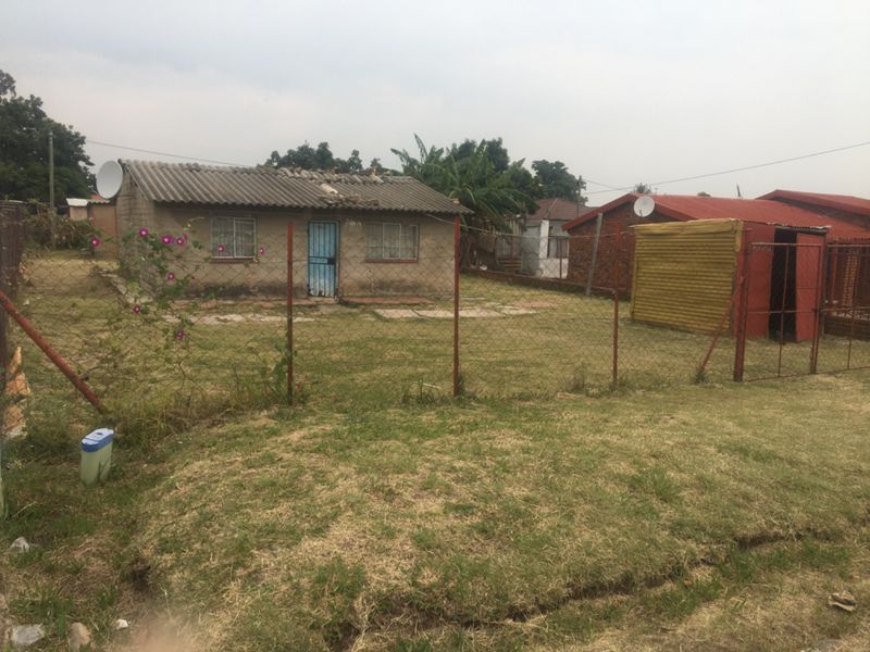 A detached residential property featuring a corrugated roof and fenced yard, showing signs of significant wear and requiring maintenance.