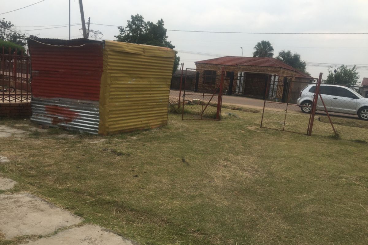 A backyard area featuring a corrugated metal shed and wire fencing, with a view of the neighboring property.