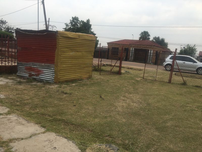 A backyard area featuring a corrugated metal shed and wire fencing, with a view of the neighboring property.