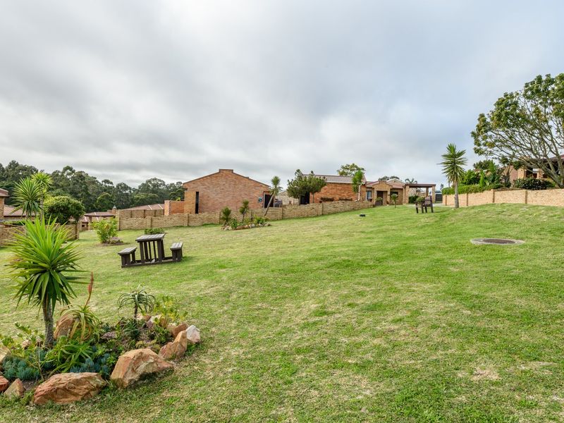 A spacious communal garden area featuring well-maintained lawns, established landscaping, and brick boundary walls within a townhouse complex.