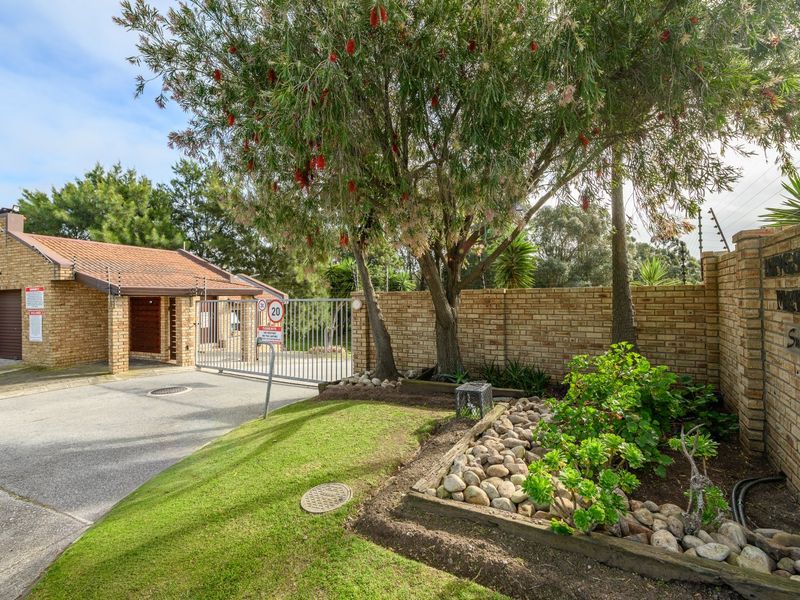Front entrance view of the townhouse complex featuring a secure automated gate, face-brick boundary walls, electric fencing, and a paved driveway.