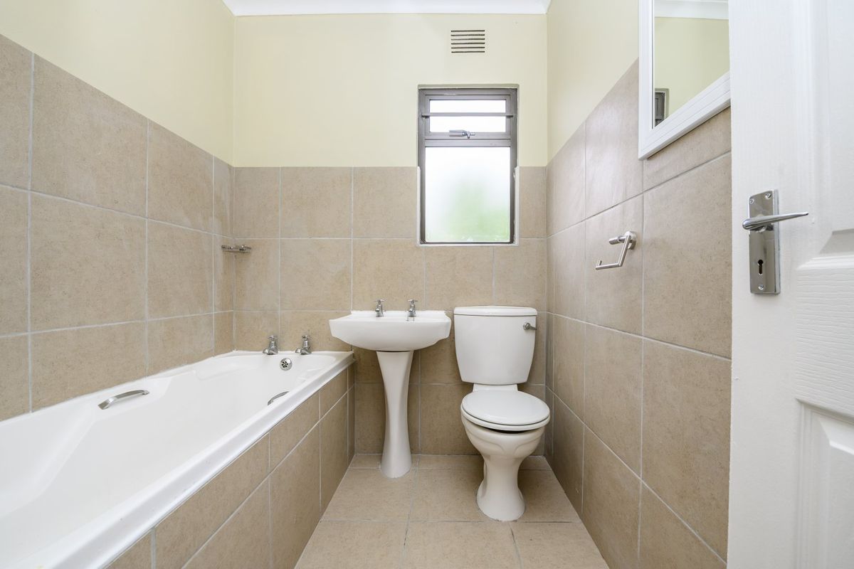A functional bathroom featuring a bathtub, pedestal basin, and toilet with neutral wall and floor tiling.