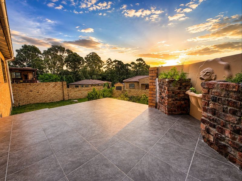 A spacious tiled patio area featuring a decorative brick water feature and views over the surrounding residential estate at sunset.