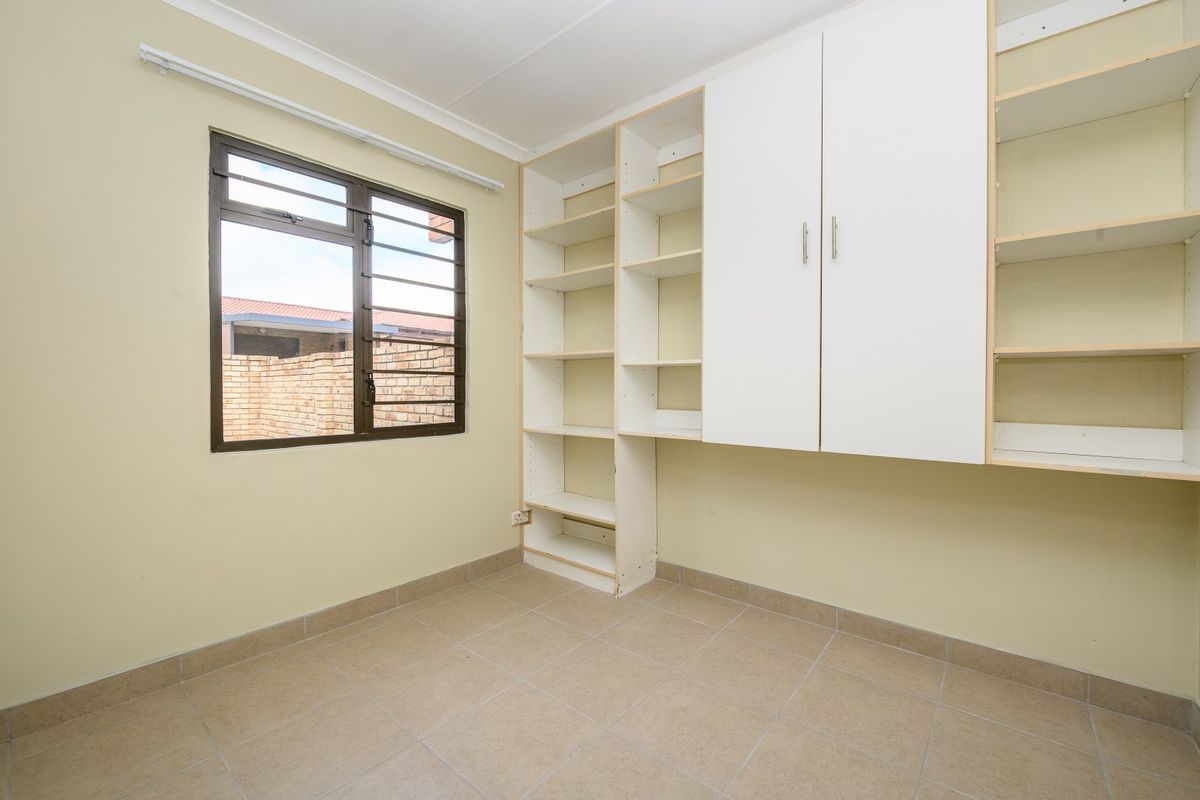 An empty bedroom featuring tiled flooring, built-in storage cupboards, and open shelving units with a window providing natural light.
