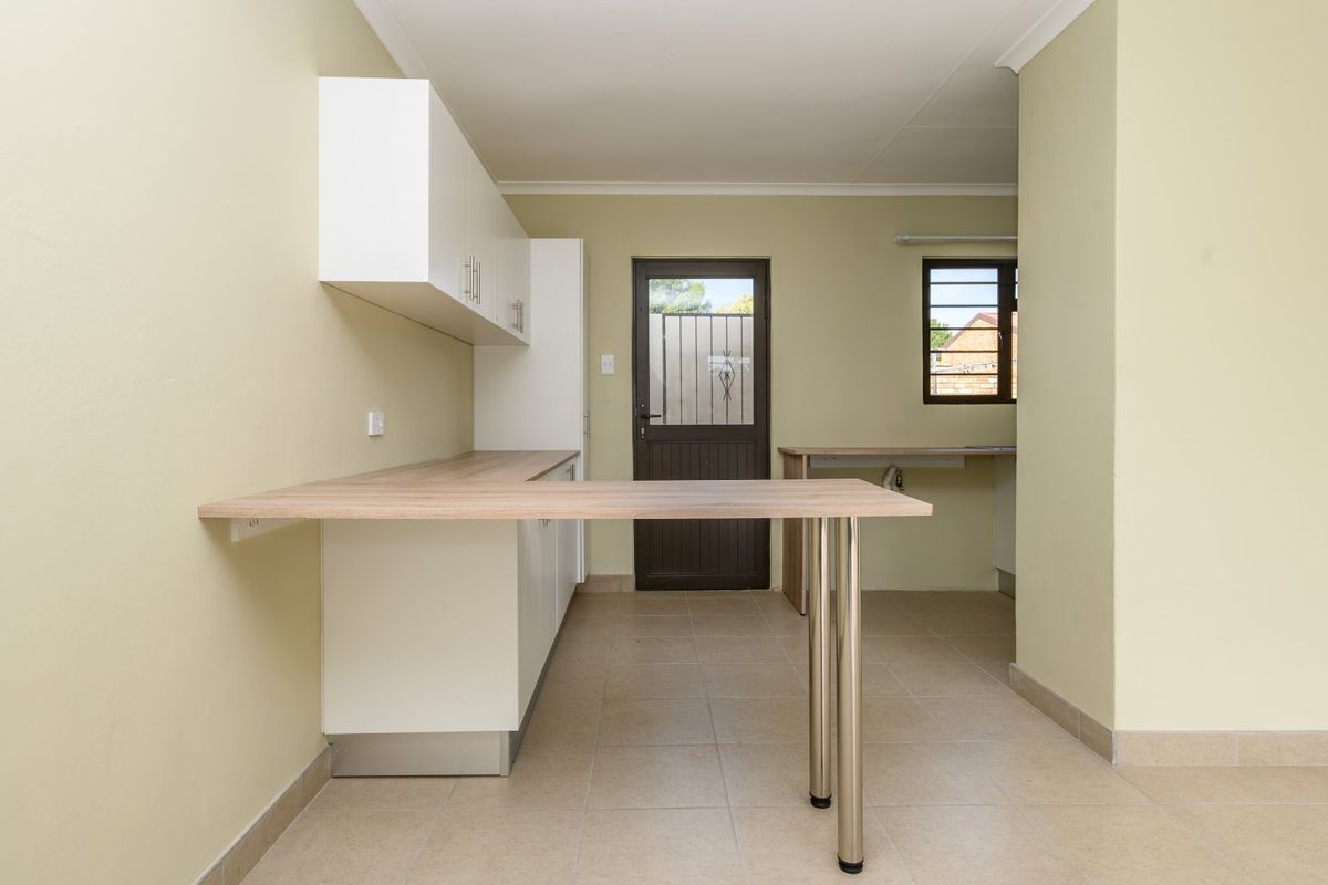 A clean, empty kitchen area featuring built-in white cabinetry, light wood-look countertops, tiled flooring, and direct access to the exterior via a security door.