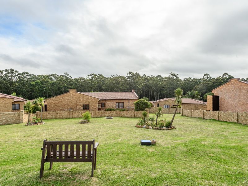 A spacious, well-maintained communal garden area featuring brick boundary walls and views of the surrounding townhouse complex and forest backdrop.
