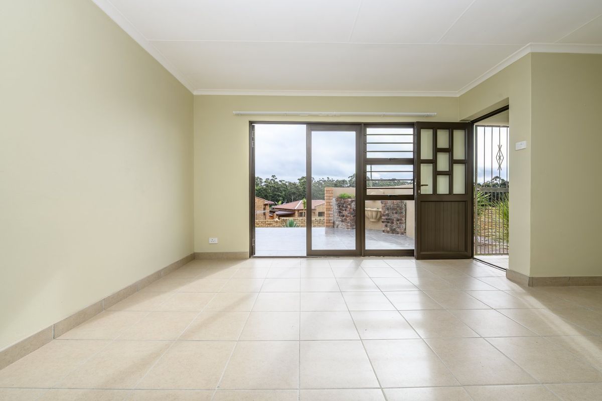A bright, empty living room featuring neutral tiled flooring and a sliding glass door that opens onto an outdoor patio area.