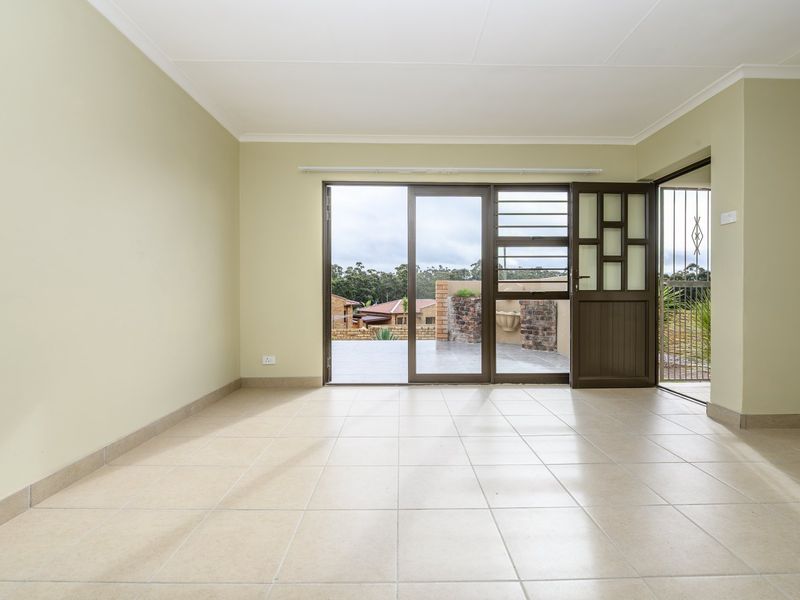 A bright, empty living room featuring neutral tiled flooring and a sliding glass door that opens onto an outdoor patio area.