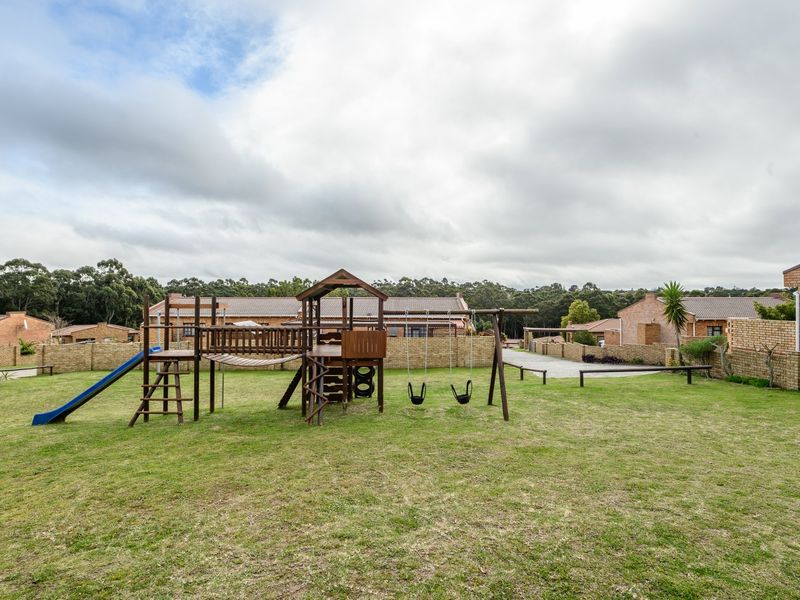 A communal garden area within a townhouse complex featuring a lawn and fixed playground equipment, enclosed by brick boundary walls.