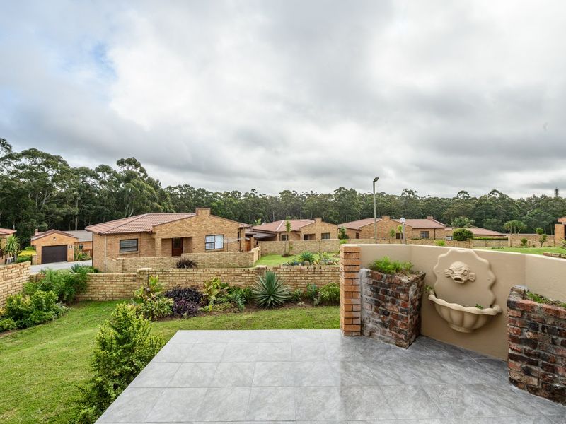 A well-maintained tiled patio featuring a decorative wall fountain, overlooking a landscaped garden and the surrounding townhouse complex.