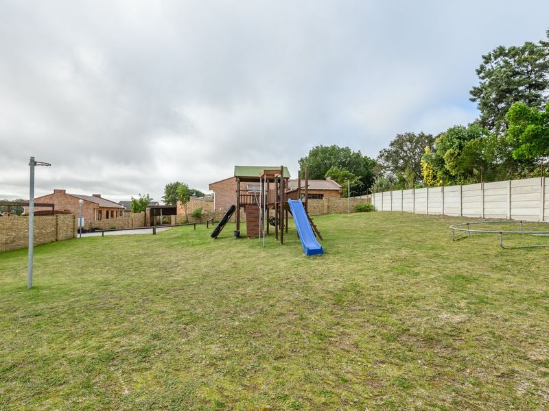 A spacious, open backyard area featuring a large lawn, enclosed by a combination of brick and precast concrete boundary walls.