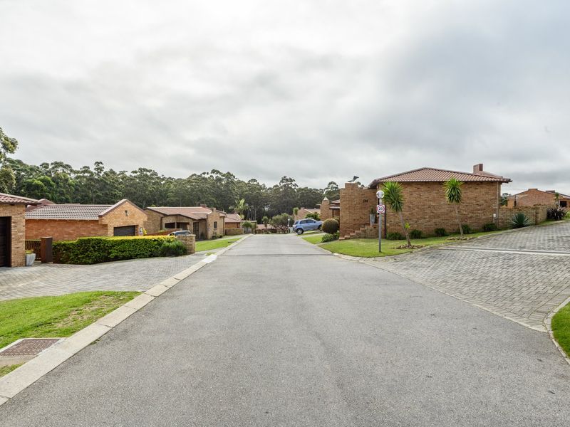A view of a residential street within a townhouse complex, featuring brick-faced homes with tiled roofs and paved driveways.