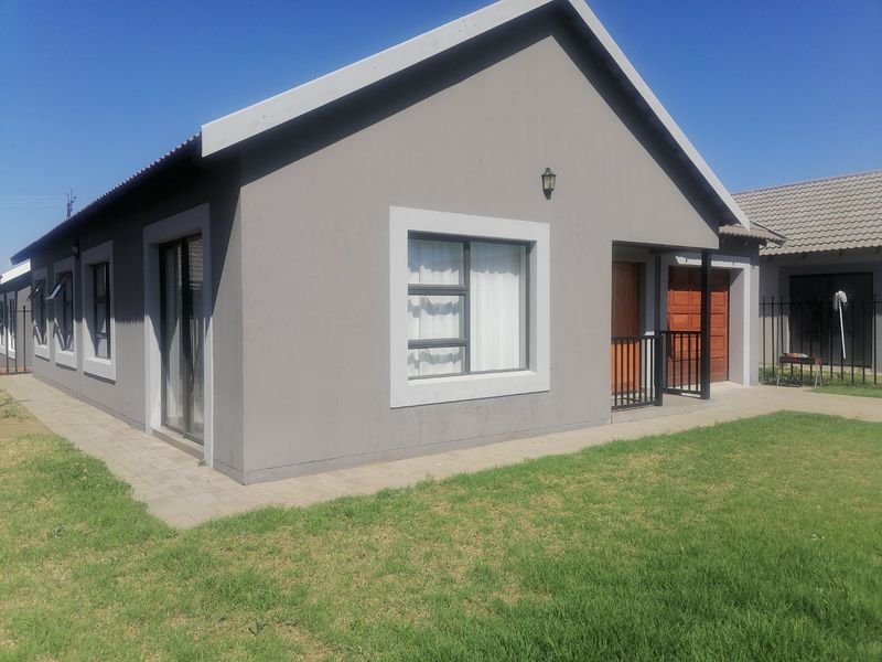 A modern single-story house exterior featuring grey rendered walls, aluminium window frames, a paved walkway, and a small front lawn.