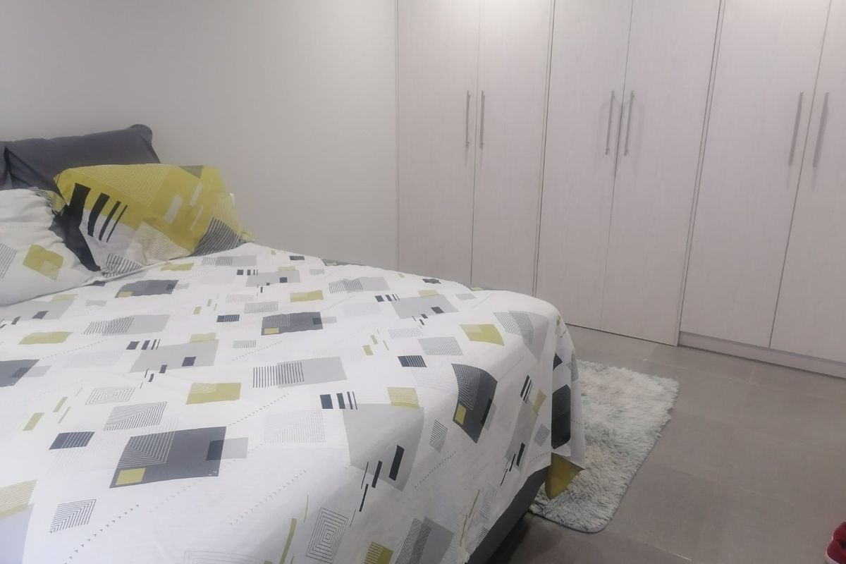 A clean and modern bedroom featuring neutral tiled flooring and extensive floor-to-ceiling built-in cupboards for ample storage.