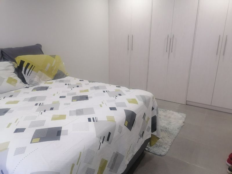 A clean and modern bedroom featuring neutral tiled flooring and extensive floor-to-ceiling built-in cupboards for ample storage.