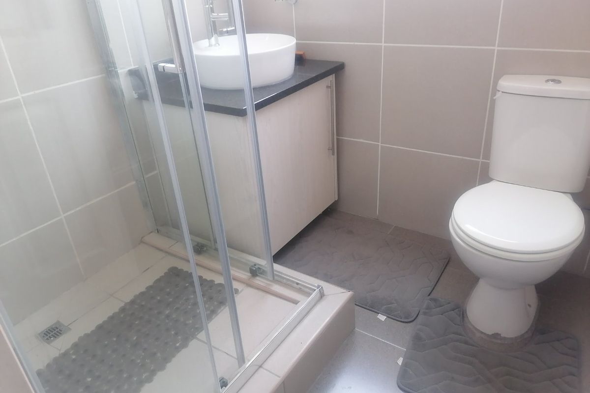A compact bathroom featuring a glass shower enclosure, a modern vessel sink with a vanity cabinet, and a standard toilet with neutral wall tiling.