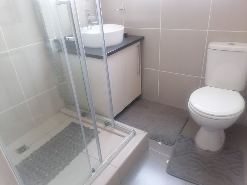 A compact bathroom featuring a glass shower enclosure, a modern vessel sink with a vanity cabinet, and a standard toilet with neutral wall tiling.