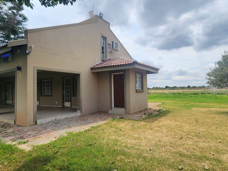 Rear view of the house featuring a spacious covered patio, paved walkway, and well-maintained garden area with mature trees.