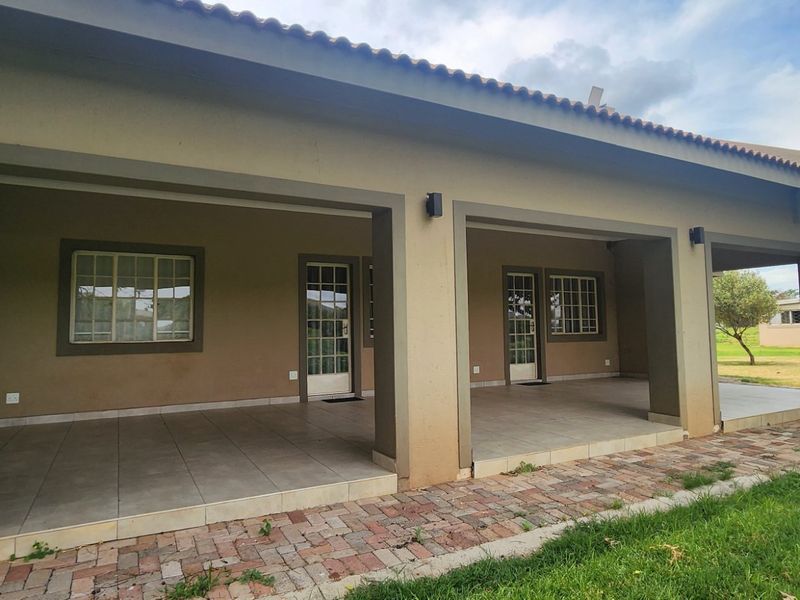 A spacious covered patio featuring tiled flooring and brick paving, providing direct access to the garden through multiple sets of french doors.