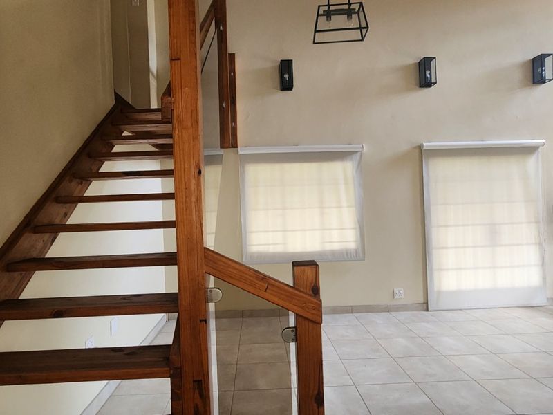 Spacious living area featuring high ceilings, tiled flooring, and a prominent wooden staircase with a matching balustrade.