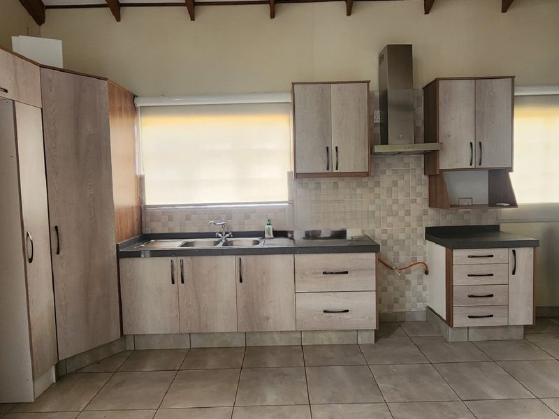 A functional kitchen featuring light wood-look cabinetry, a stainless steel extractor fan, tiled backsplash, and exposed timber ceiling beams in an open-plan layout.