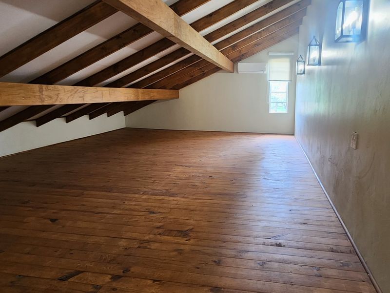 An empty attic-style bedroom featuring exposed timber beams, polished timber flooring, and wall-mounted lighting.