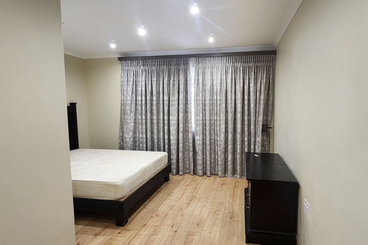 A spacious bedroom featuring light-toned laminate flooring, recessed ceiling lighting, and full-length curtain tracks.