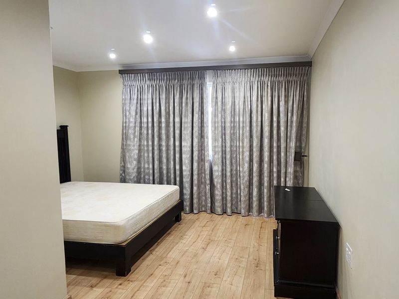 A spacious bedroom featuring light-toned laminate flooring, recessed ceiling lighting, and full-length curtain tracks.