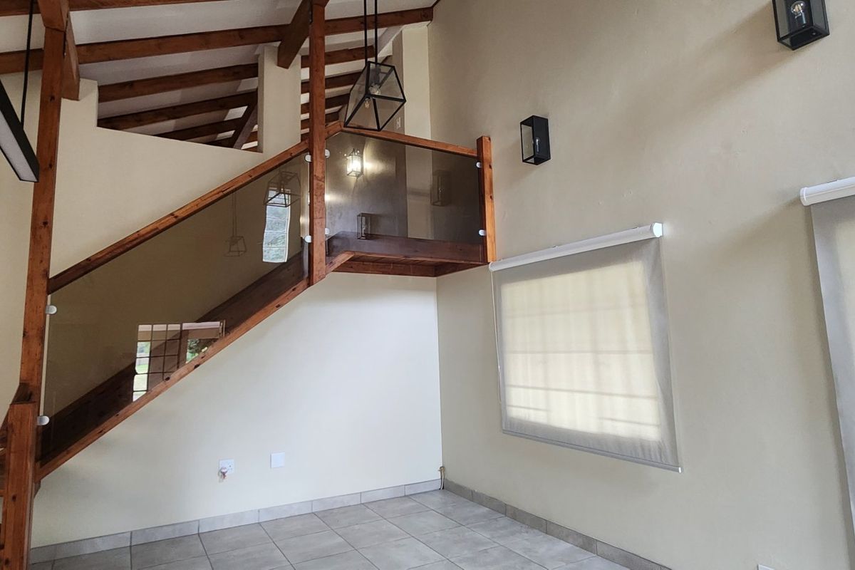 Spacious living area featuring high vaulted ceilings with exposed timber beams, a modern timber staircase with glass balustrade, and neutral ceramic floor tiling.