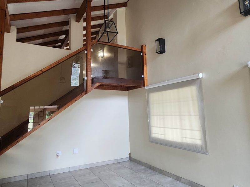 Spacious living area featuring high vaulted ceilings with exposed timber beams, a modern timber staircase with glass balustrade, and neutral ceramic floor tiling.