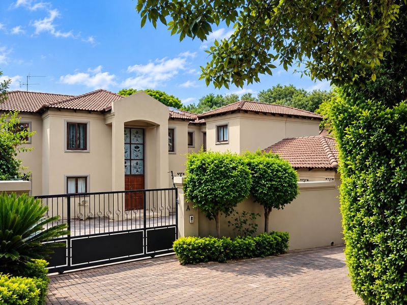 A well-maintained double-story residence featuring a tiled roof, secure wrought iron gate, and a paved driveway with established garden landscaping.